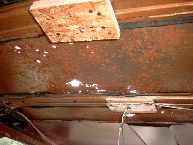Rusted interior roof of a vehicle with water stains and wood bracing. Wires are visible
