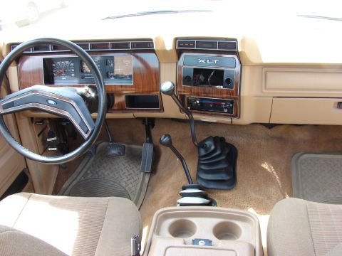 1984 Ford F-250 - The dashboard and center console of a truck, showing the steering wheel, gauges, and manual transmission shifters.