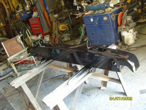 1989 Ford Bronco - A shiny black bumper is propped up on sawhorses in a workshop, with tools and equipment visible in the background.