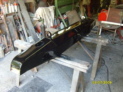1989 Ford Bronco - A black bumper with gold trim and circular cutouts is displayed in a workshop setting.
