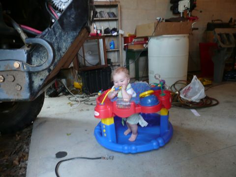 1990 Ford Bronco - A baby plays in a colorful activity center inside a garage, with vehicle parts visible.