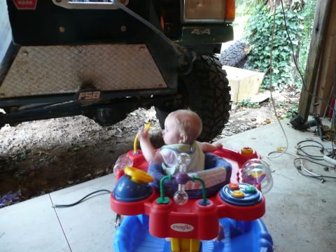 1990 Ford Bronco - A baby sits in a walker, positioned in front of the bumper and tire of a green vehicle.