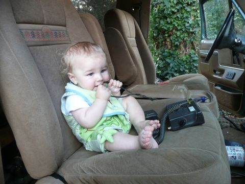 1990 Ford Bronco - A baby sits in the passenger seat of a vehicle, playing with a cord near a CB radio.