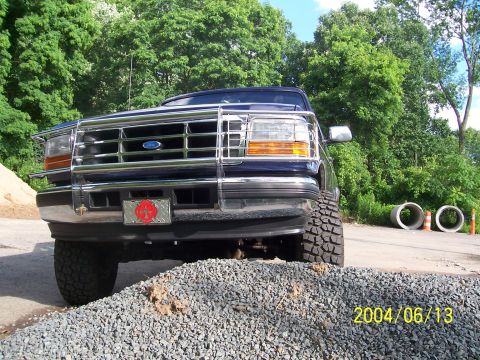 1990 Ford Bronco - Dark blue Ford Bronco with a chrome bull bar and off-road tires is parked on a gravel pile.
