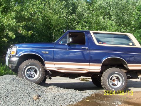 1990 Ford Bronco - This blue Ford Bronco is parked on a gravel surface with trees in the background.