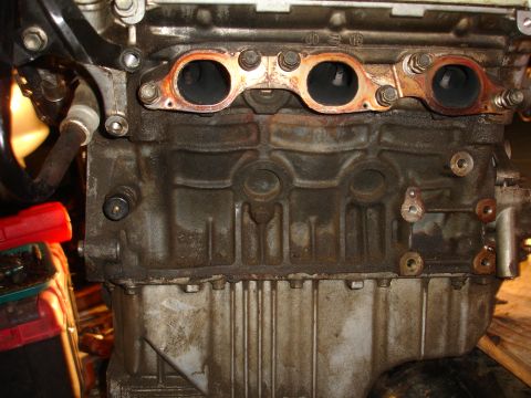 1990 Ford Taurus - The engine block shows signs of wear and oil residue around the exhaust manifold area.