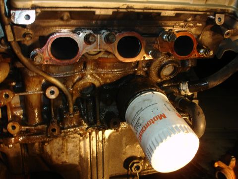 1990 Ford Taurus - Close-up of an engine block showing an oil filter and exhaust manifold, with visible oil residue.