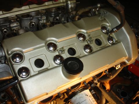 1990 Ford Taurus - Close-up of an engine valve cover, showing chrome bolt caps and a black rubber plug.