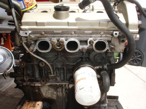 1990 Ford Taurus - Close-up view of an engine block, an oil filter and exhaust ports. The registry claims it is a 1990 Ford Taurus, but this is unconfirmed.
