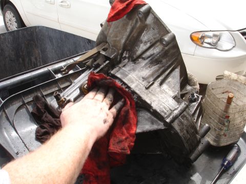 1990 Ford Taurus - A person is cleaning a dirty transmission with a red cloth. A white minivan is visible in the background.