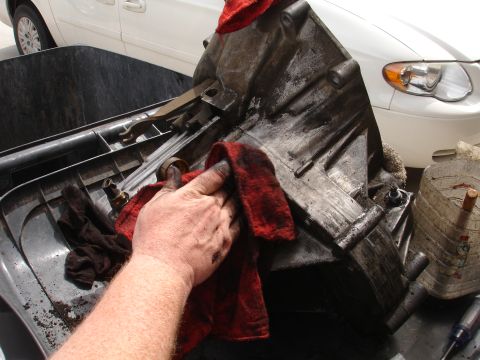 1990 Ford Taurus - A greasy transmission part is cleaned with a red rag, with a white minivan visible behind it.