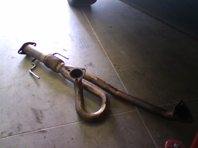 Used exhaust downpipe with catalytic converter on a concrete garage floor