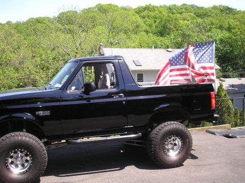 1995 Ford Bronco - A black Ford Bronco is parked in front of a house with two American flags displayed in its bed.