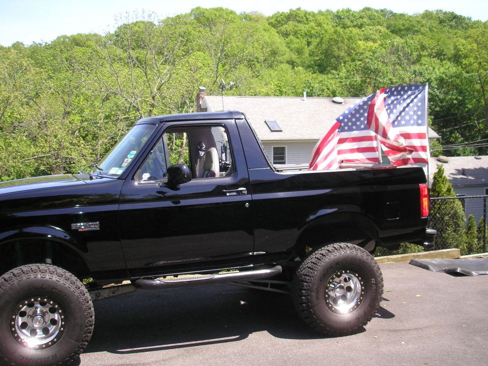 Black 1995 Ford Bronco with American flags in the bed, parked outside