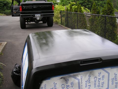 1995 Ford Bronco - A black pickup truck is parked behind a black vehicle top, with a fence and trees in the background.