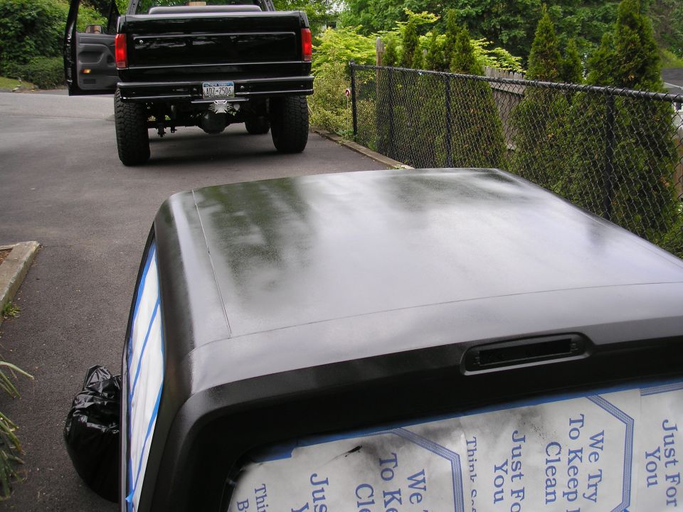 SUV hardtop masked with tape and paper being repainted flat black on a driveway