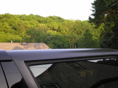 1995 Ford Bronco - Vehicle roofline and window reflection showing a house and trees against a bright sky.