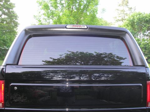 1995 Ford Bronco - The rear of a black SUV is shown with a reflection of trees in the window.