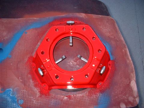 1970 Ford Torino - Clutch pressure plate, painted red, sits on a textured surface with overspray.