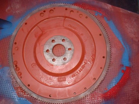 1970 Ford Torino - A red painted flywheel with a toothed outer edge is shown, centered on a red and blue speckled surface.