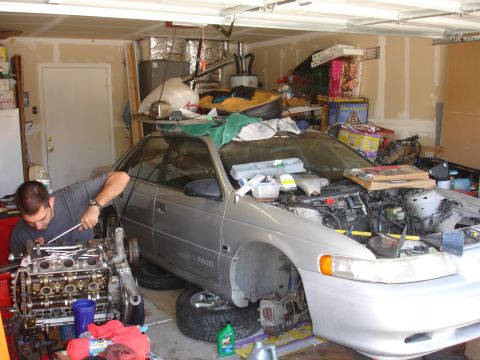 1992 Ford Taurus - Man works on a 1992 Ford Taurus engine during a rebuild in a busy garage.