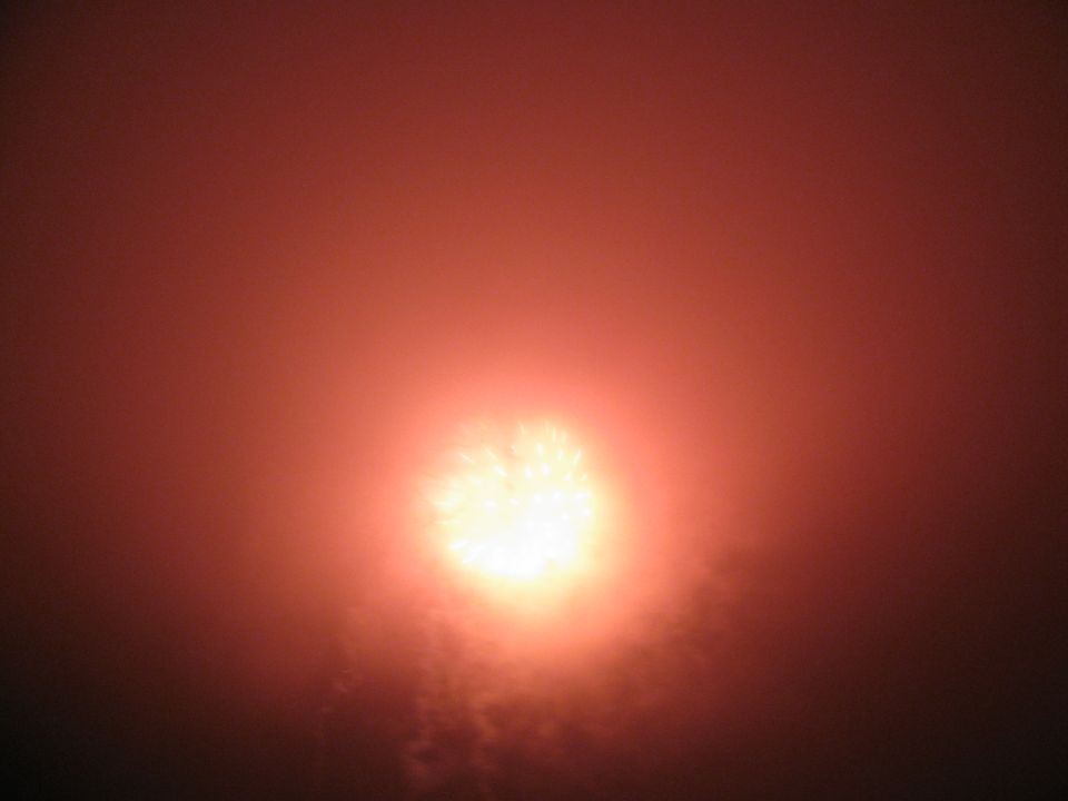 Bright fireworks explode in a reddish-orange sky