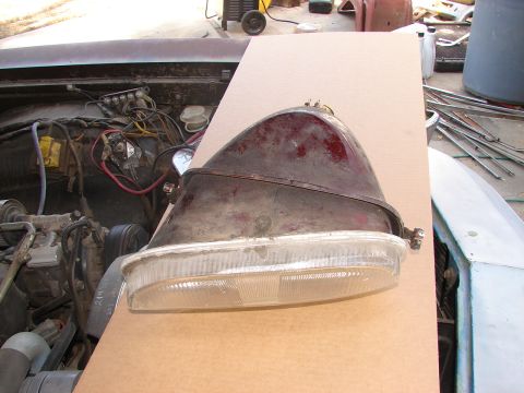 1973 Ford Ranchero - A detached headlight assembly sits on cardboard, partially obscuring the engine bay of a vehicle.