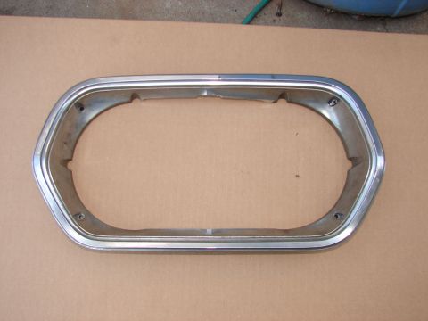 1973 Ford Ranchero - A single chrome headlight bezel is shown against a brown background, with visible mounting points and some damage.
