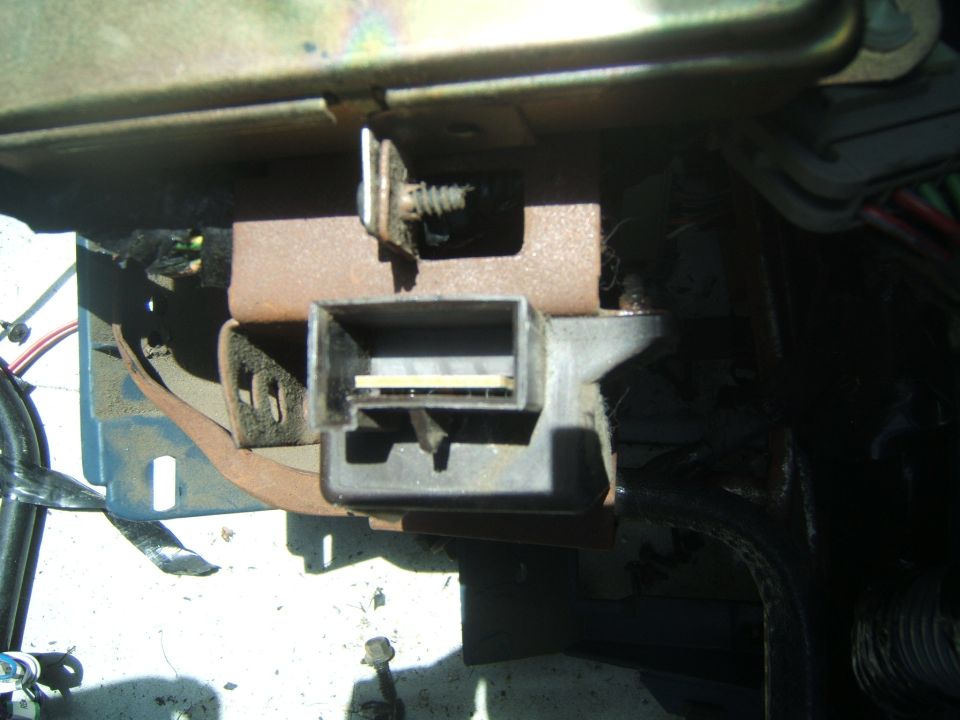 close-up of a gray plastic connector with wires behind it, attached to a rusty bracket