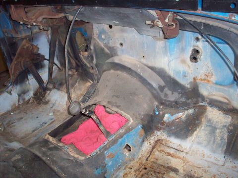 1978 Jeep CJ5 - The interior of a blue vehicle, showing the floor pan, pedals, and shifter mechanism, with visible rust and exposed metal.