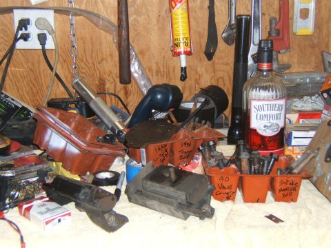 1988 Ford Bronco - A cluttered workbench displays engine components, tools, and a bottle of Southern Comfort.