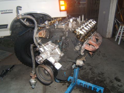 1988 Ford Bronco - Engine removed from a white truck, possibly a Ford Bronco, sits on a stand for work.