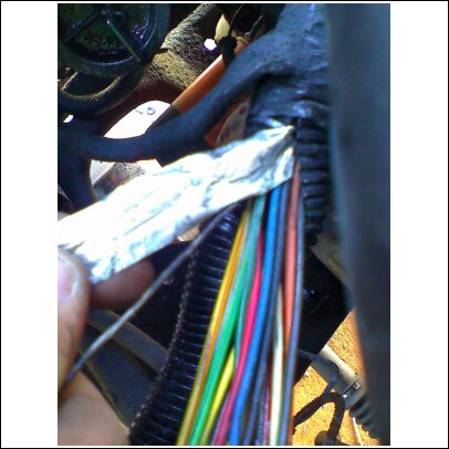 1989 Ford F-150 - A close-up view of a vehicle's wiring harness, with a hand partially covering some of the wires with foil.