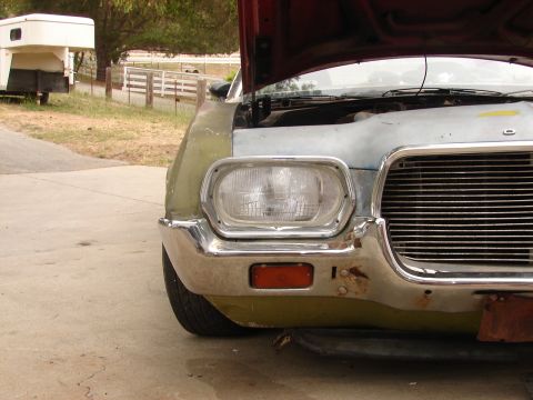 1973 Ford Ranchero - The front of a car, possibly a Ford Ranchero, is shown with its hood open. The vehicle appears to be in a state of disrepair.