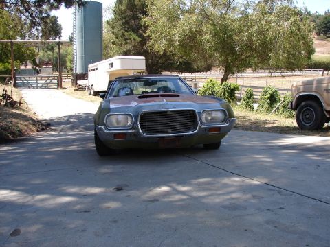 1973 Ford Ranchero - A weathered coupe utility with a distinctive grille and hood scoop sits in a driveway, with a horse trailer and another vehicle visible.