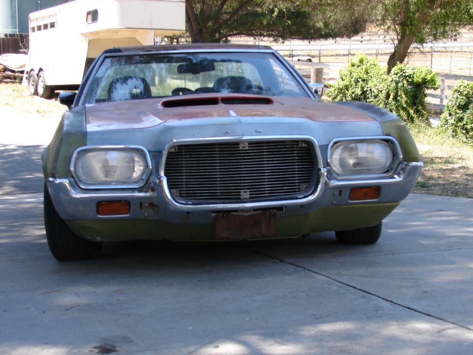 Front view of green primered 1970s Ford project car with chrome grille and hood scoop, bumper removed