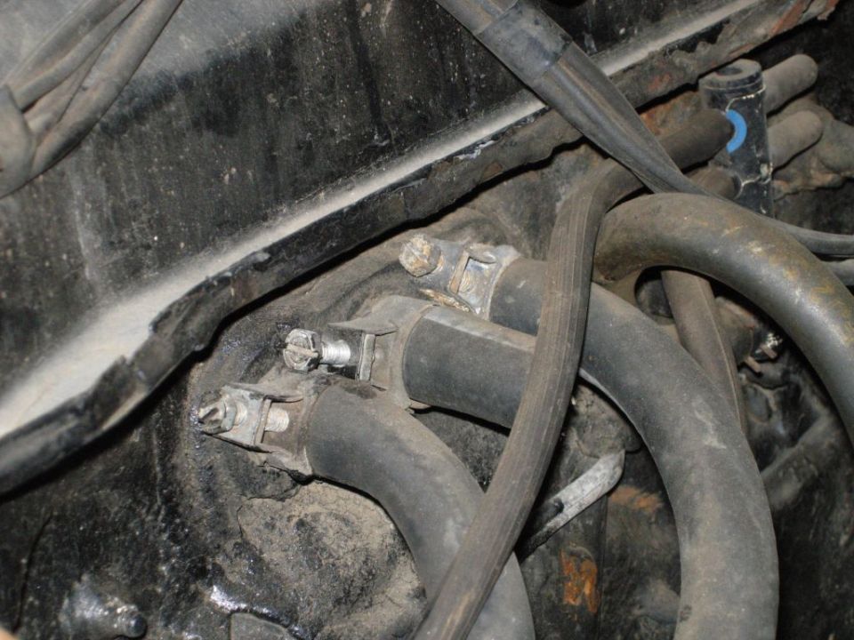 Engine hoses and metal clamps secured to a black metal surface, with visible wiring