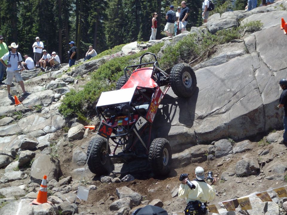 Red off-road buggy with large tires climbing a rocky incline, number 12 visible