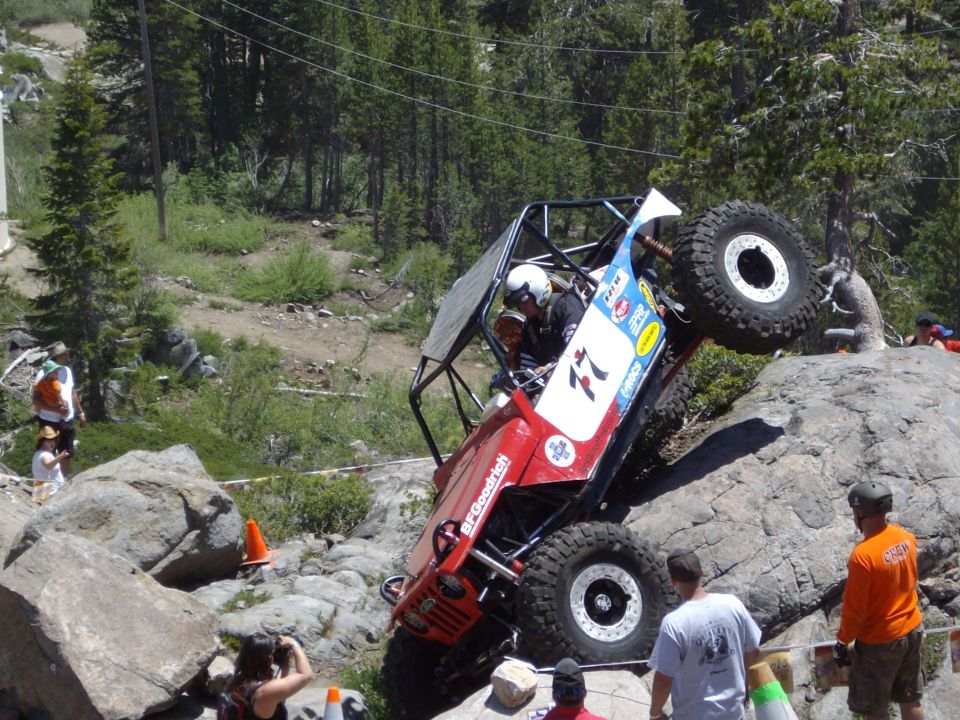 Red off-road vehicle with a roll cage climbing over rocks, BFGoodrich tires visible