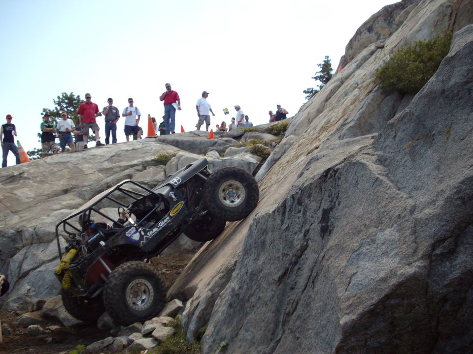 Off-road vehicle climbing steep rock face with spectators watching