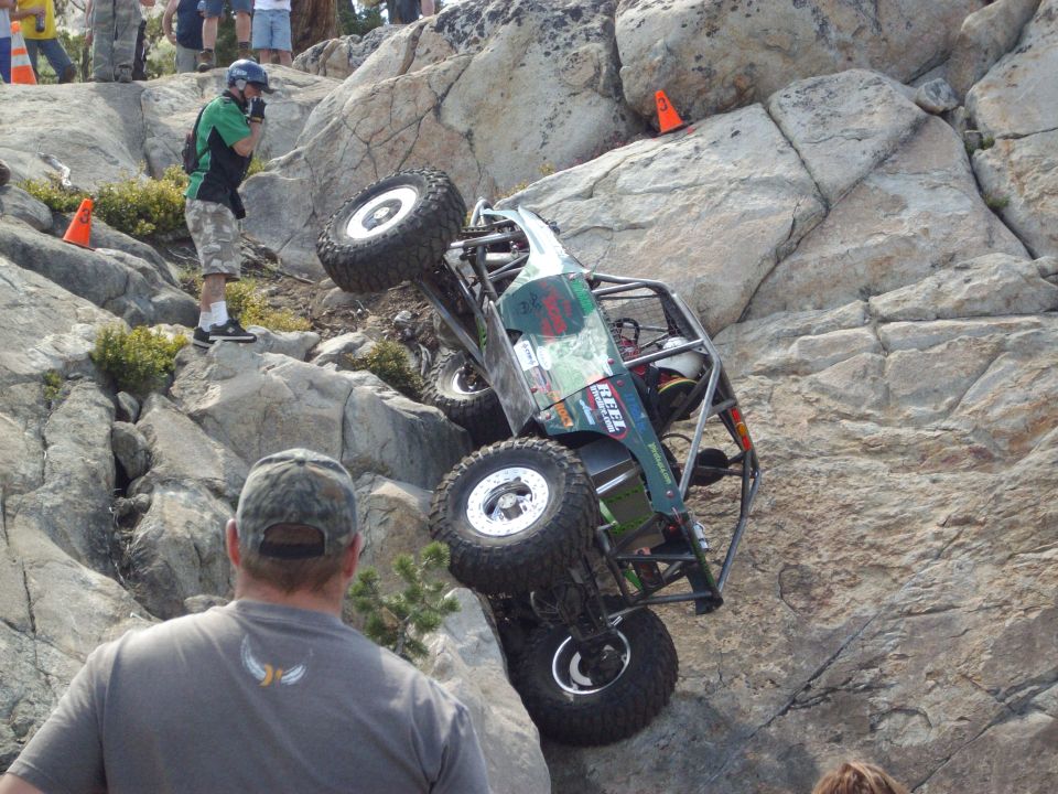 Off-road buggy is tilted on a rocky incline with spectators watching