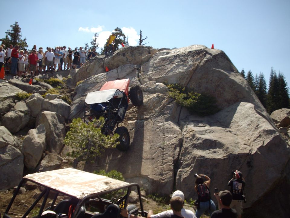 Off-road vehicle climbing a rocky incline with spectators watching