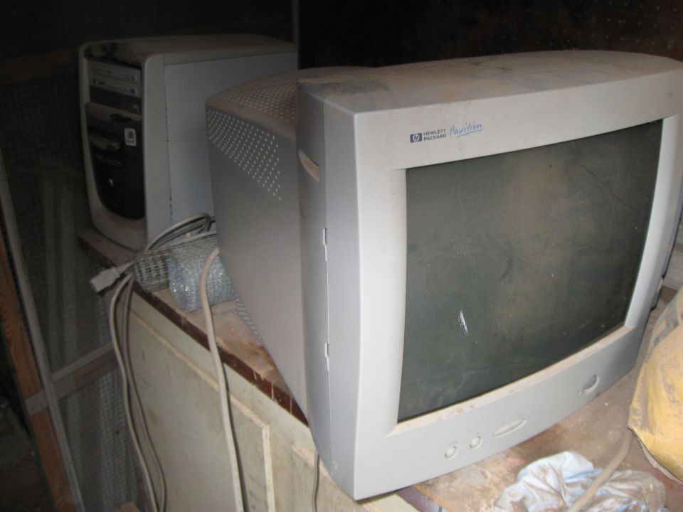 Dusty Hewlett-Packard Pavilion monitor and a beige computer tower sit on a cluttered surface