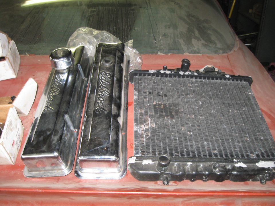 Two chrome Edelbrock valve covers and a black radiator sit on a red surface
