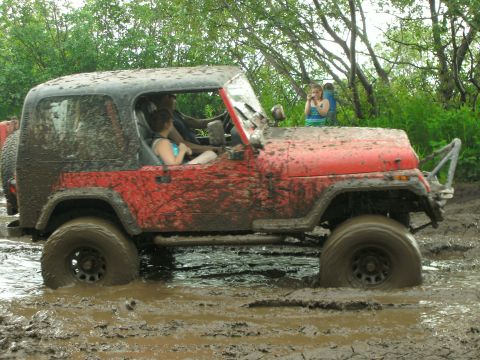 1979 Chevrolet Blazer - A red Jeep Wrangler is stuck deep in mud, with people inside and onlookers in the background. The vehicle is heavily covered in mud.