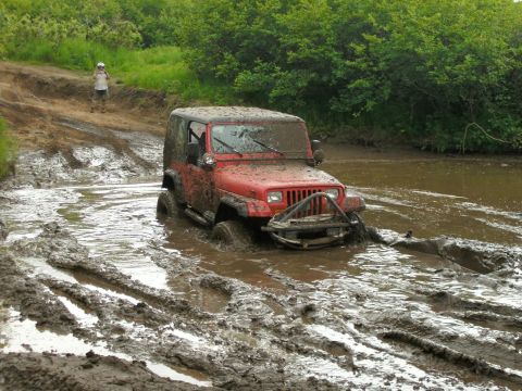 1979 Chevrolet Blazer - A red Jeep Wrangler navigates a muddy off-road trail, getting stuck in the mire.