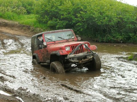 1979 Chevrolet Blazer - A red Jeep Wrangler navigates a muddy trail, with its tires deep in the water.