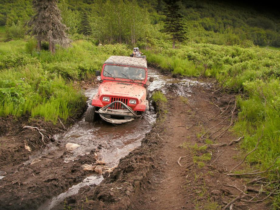 Red Jeep Wrangler navigating a muddy trail with another vehicle behind it