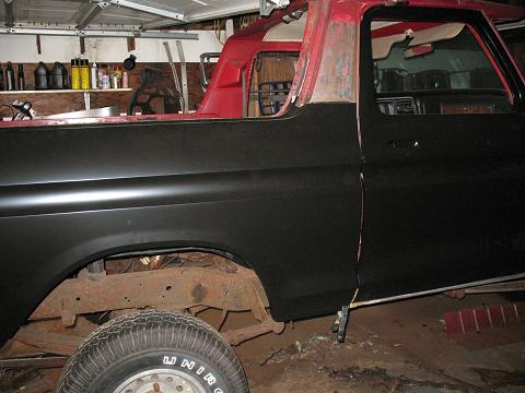 1978 Ford Bronco - A 1978 Ford Bronco is shown in a garage, undergoing restoration with a black lower body and red upper body.