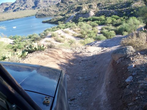 1996 Ford Bronco - Driving on a rough, dusty trail with a lake and mountains in the background.